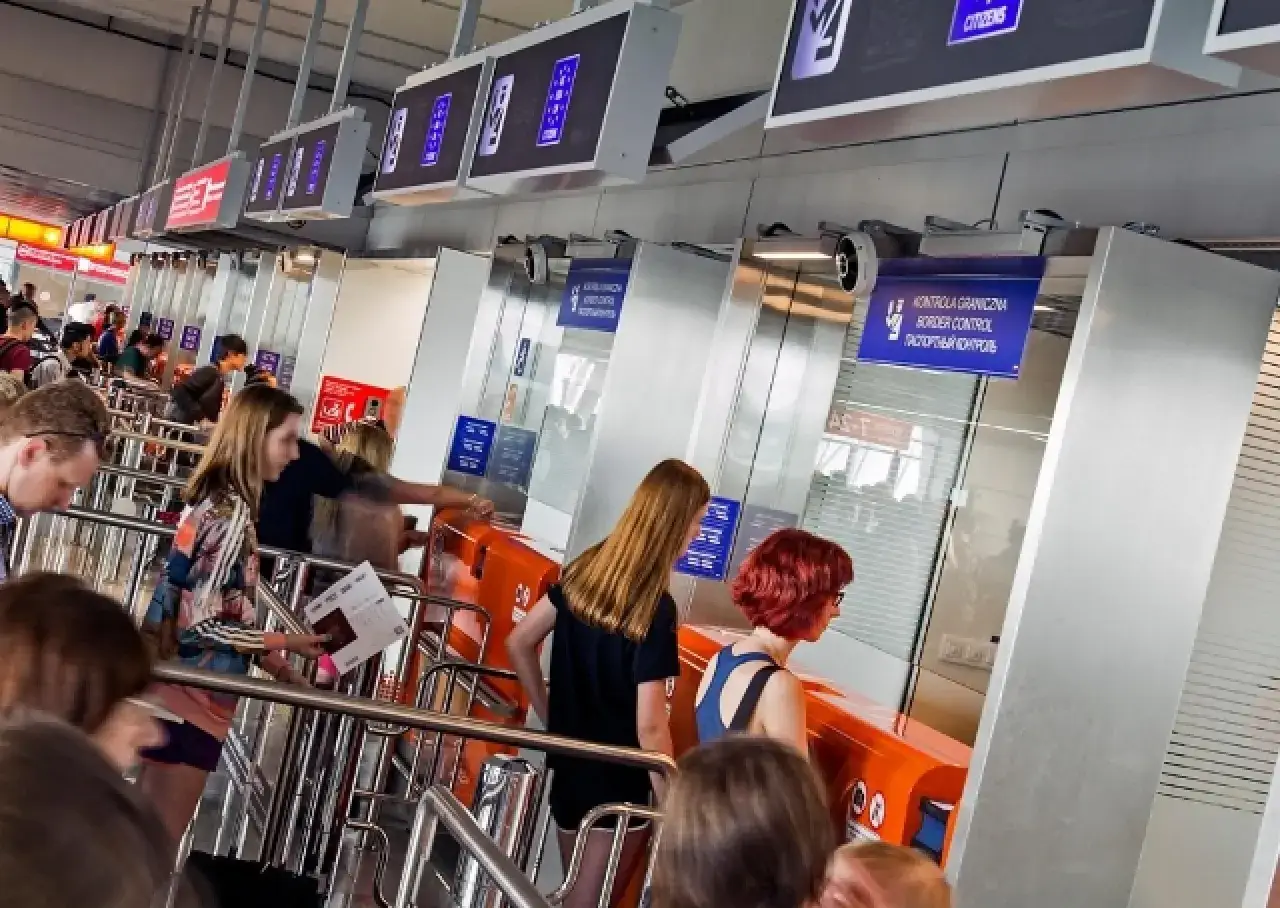 Kolejka do kontroli granicznej na lotnisku. Ludzie czekają na boarding, trzymając dokumenty.