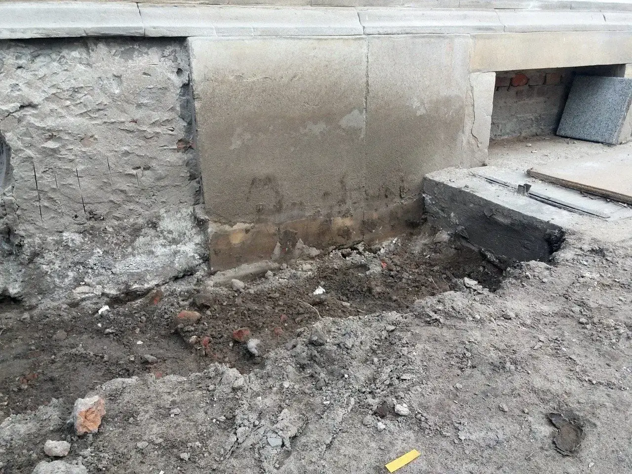 Widoczny pęknięty fundament, odsłonięta cegła i ziemia. Trwa remont.
