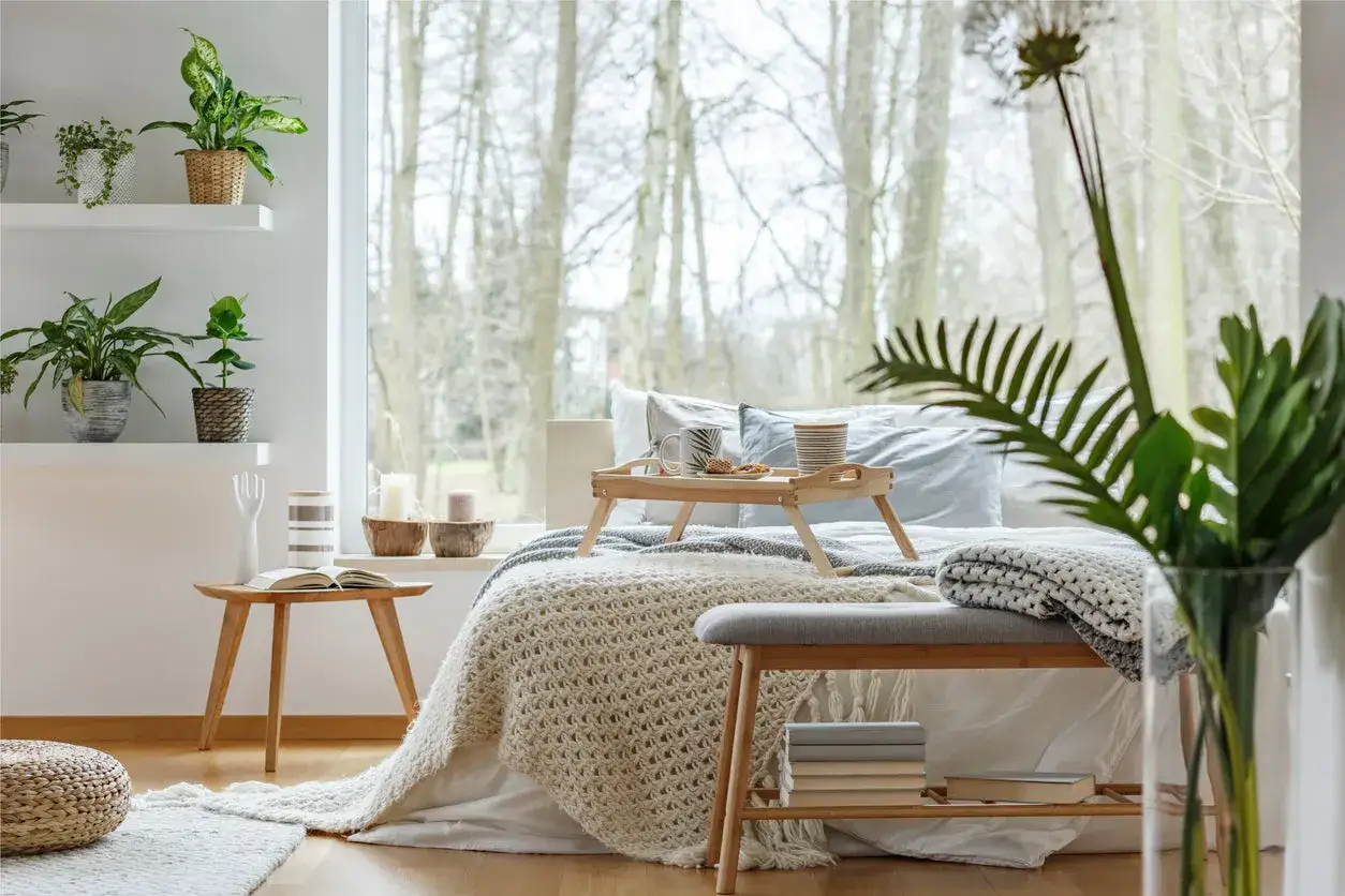 Sypialnia z elementami biophilic design: ł&oacute;żko z tacą śniadaniową, rośliny doniczkowe i widok na las.