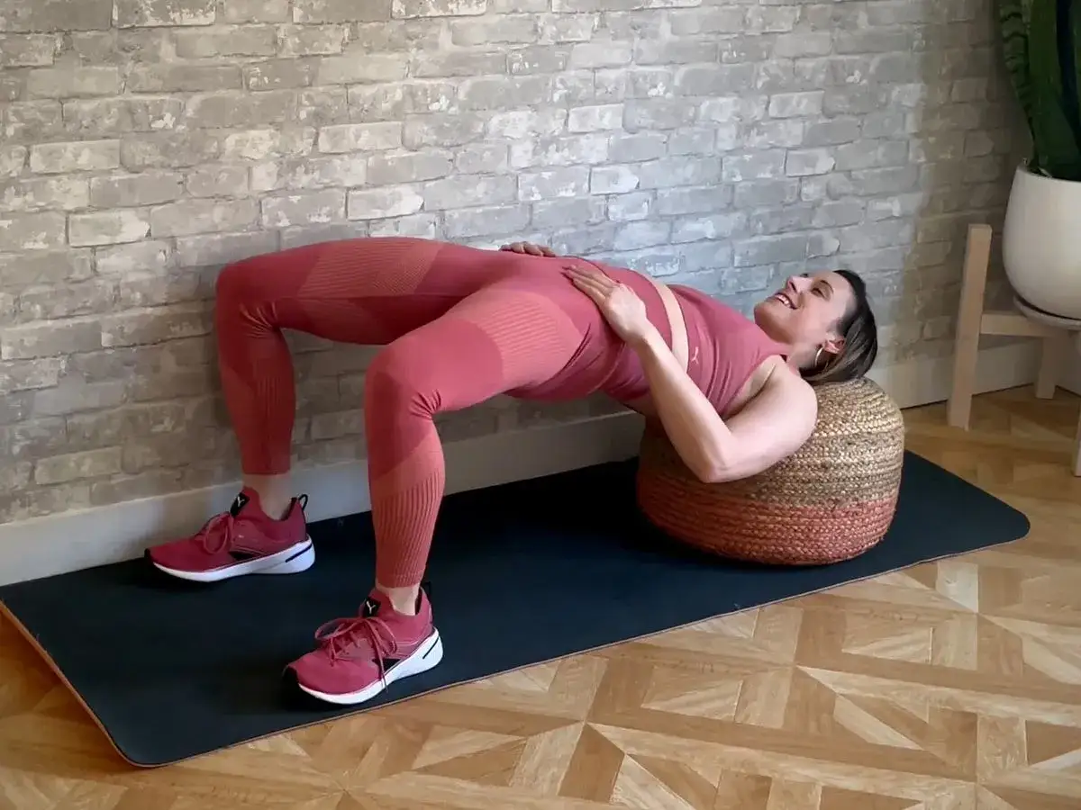 Kvinna utför hip thrust med fötterna på en pall.