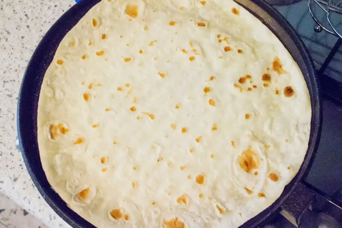 Piadina in cottura su una padella, con piccole bolle dorate che si formano sulla superficie.