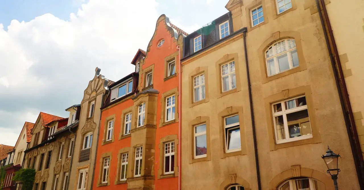 Reihe von bunten H&auml;usern, darunter ein orangefarbenes Geb&auml;ude mit verzierten Fenstern. Ein Teil der Fassade erinnert an 250 baugb.