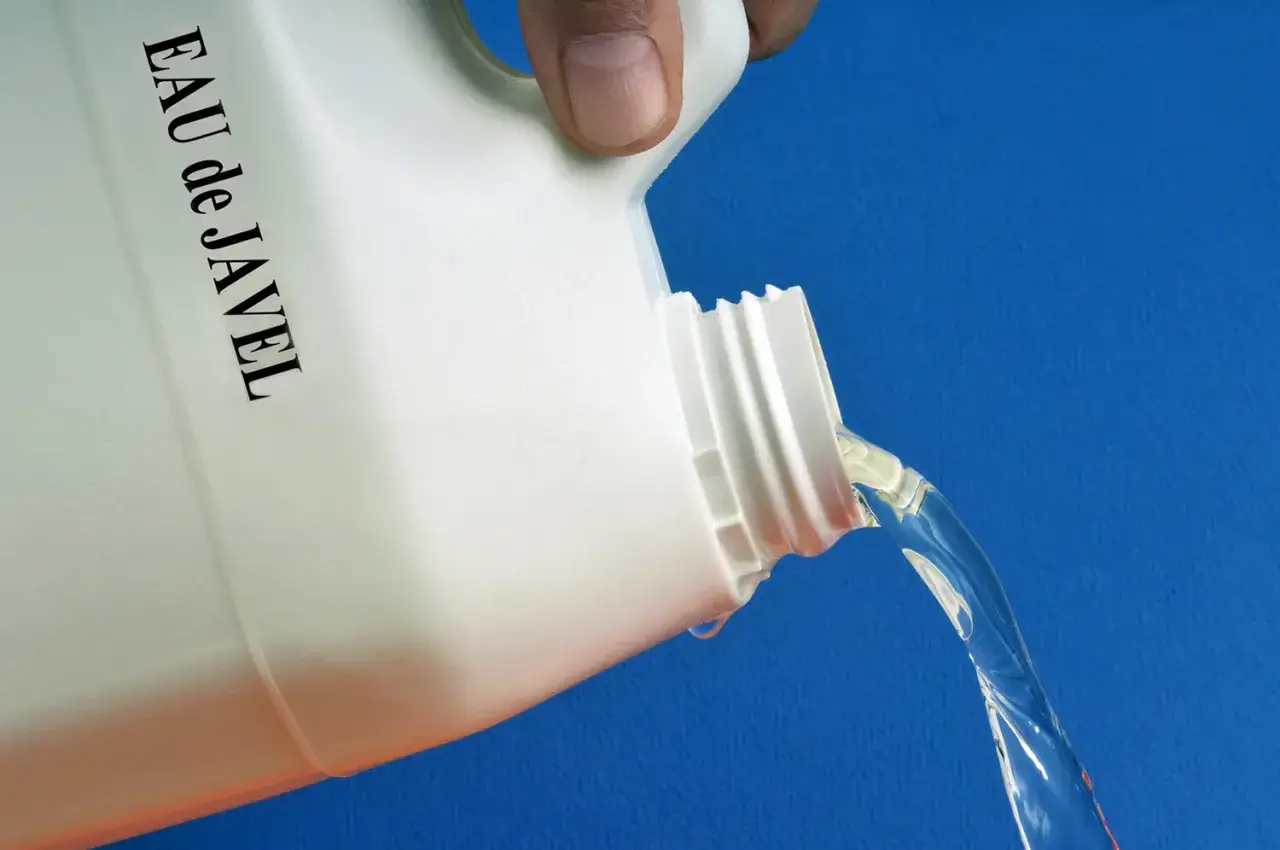 Une main verse de l'eau de Javel d'un bidon blanc. Id&eacute;al pour le nettoyage de fa&ccedil;ade.