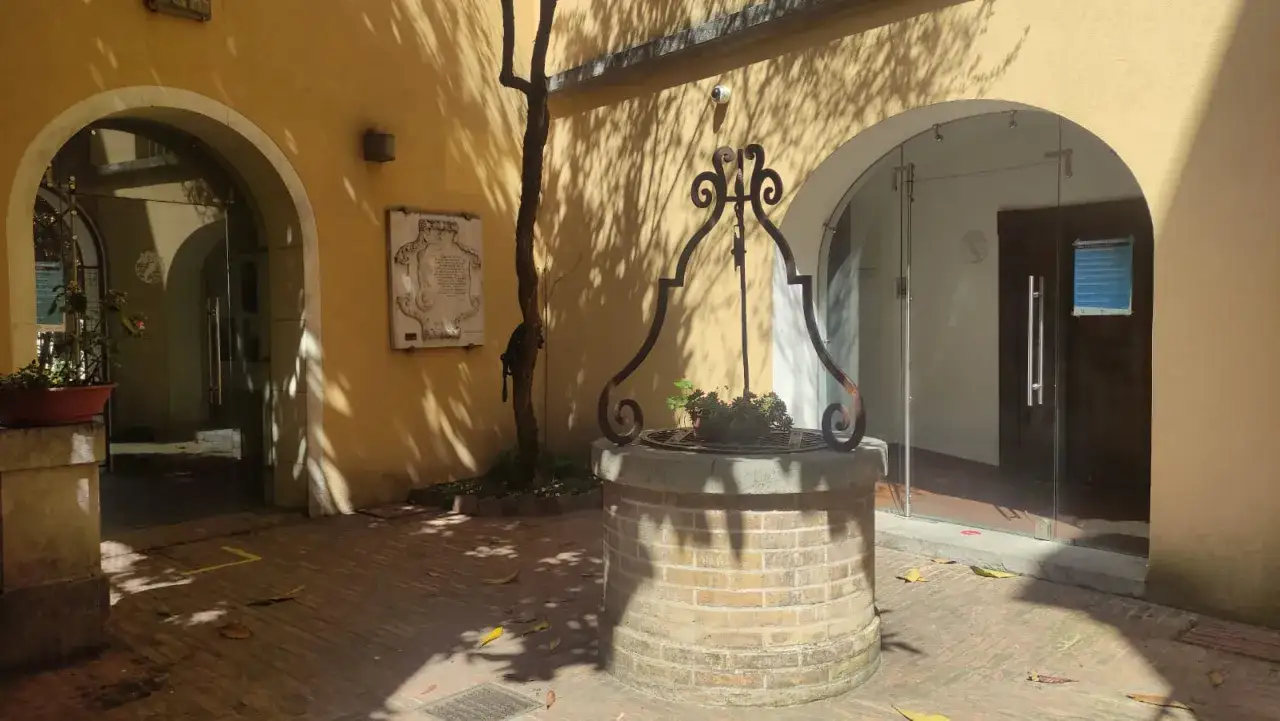 Cortile della casa di D'Annunzio con pozzo in mattoni, alberello e lapide commemorativa.