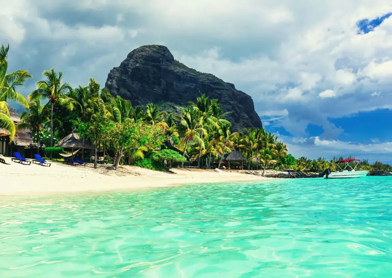 Rajska plaża na Mauritiusie z palmami, górą w tle i łodzią. Idealne miejsce na wakacje, nie potrzebujesz wizy, by tu przyjechać.