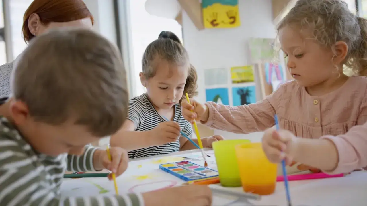 Dzieci malują farbami pod okiem nauczycielki. Ile godzin tygodniowo pracuje nauczyciel przedszkola?