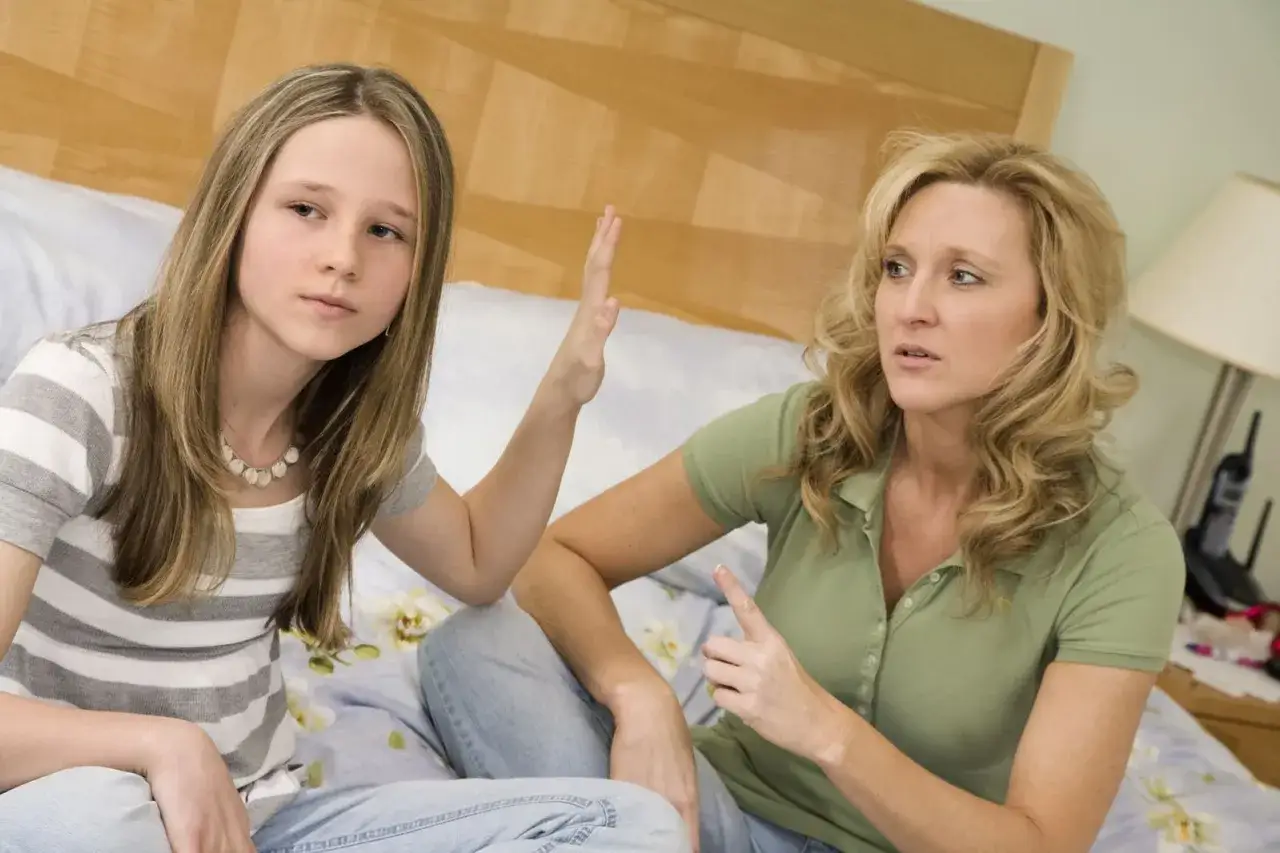 Madre e figlia discutono a letto. La figlia alza una mano, forse per fermare la madre, mostrando come comportarsi con una figlia ribelle.