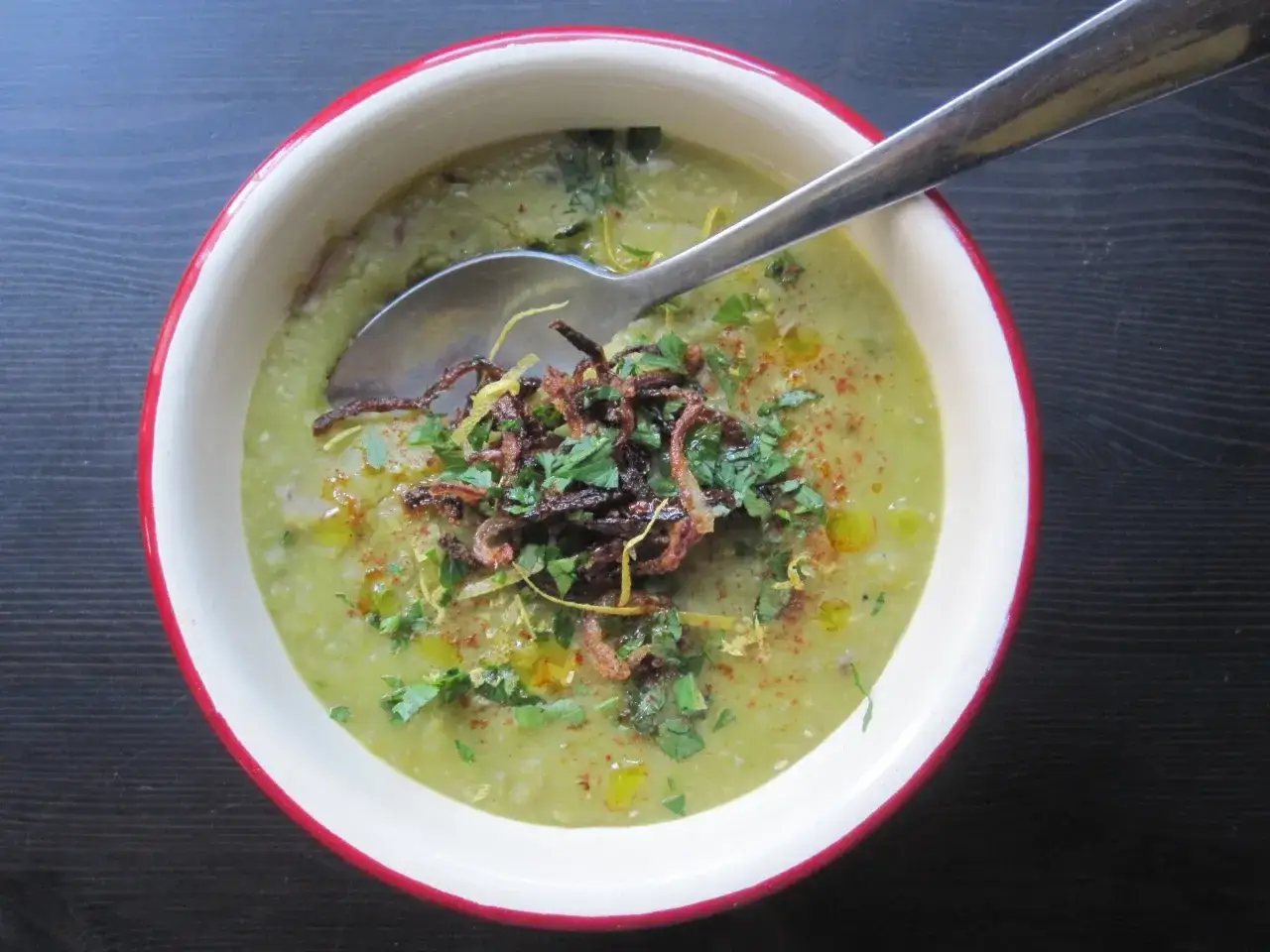Un bol de soupe de pois cass&eacute;s onctueuse, garnie d'oignons frits croustillants, de persil frais et d'un filet d'huile d'olive.