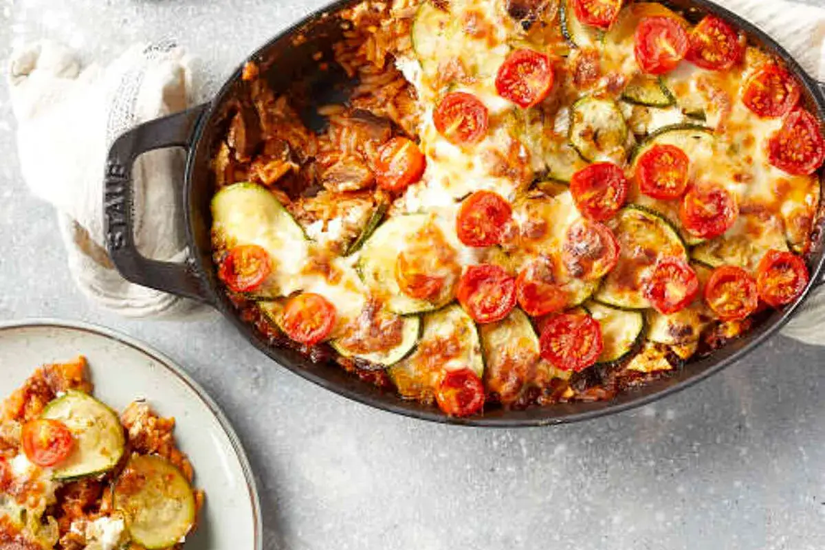 Un plat de moussaka v&eacute;g&eacute;tarienne gratin&eacute;e, garni de courgettes et de tomates cerises, servi dans une cocotte Staub.