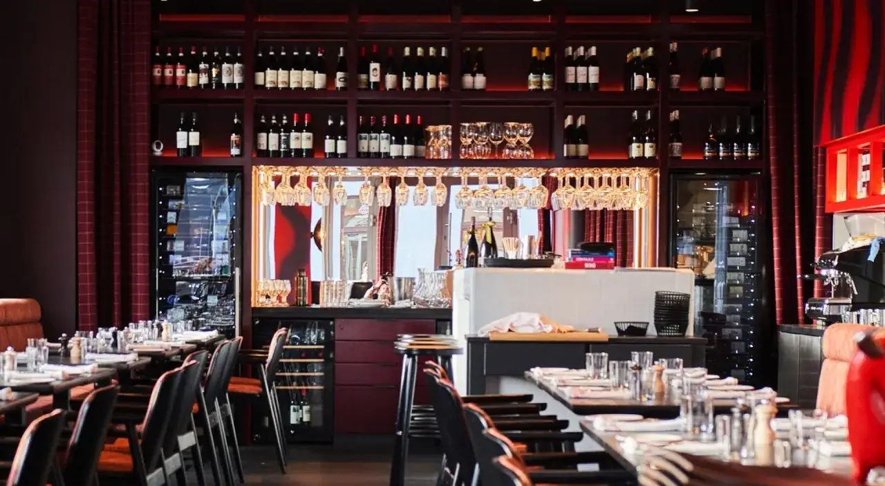 Eleganckie wnętrze restauracji z gwiazdką Michelin w Polsce. Stoły nakryte, półki uginają się od butelek wina, a nad barem wiszą kieliszki.
