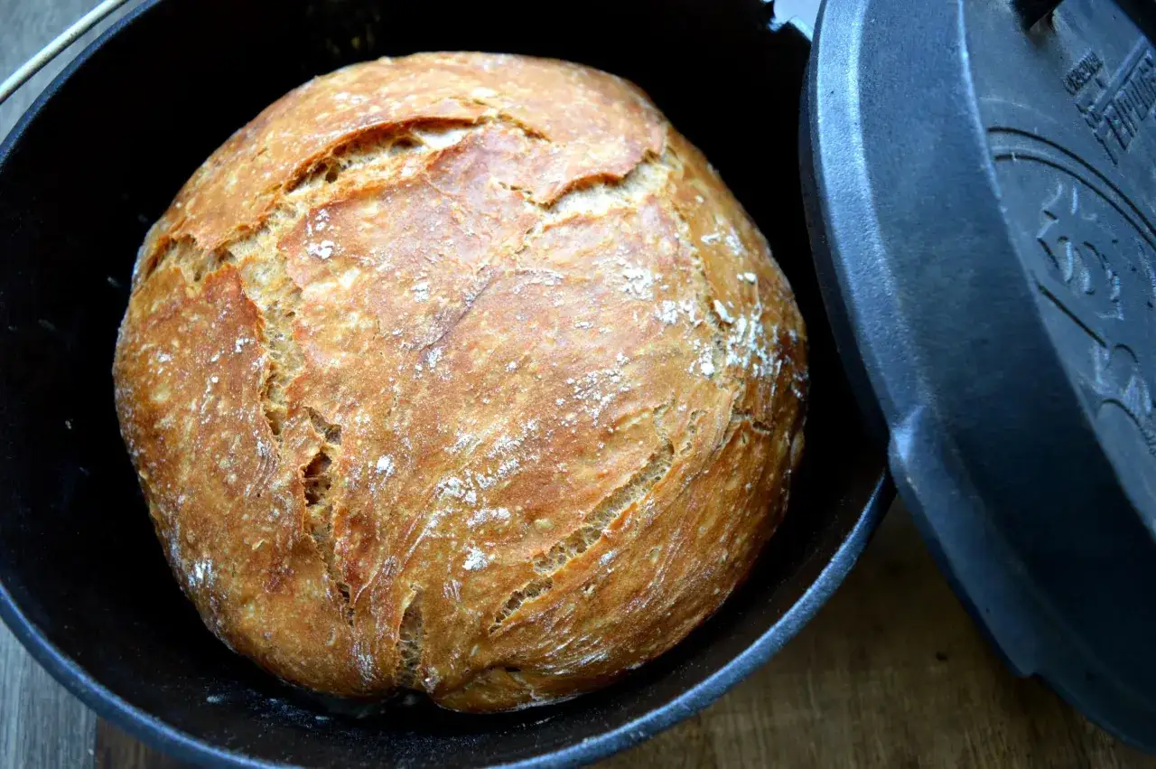 Frisch gebackenes, goldbraunes Brot mit knuspriger Kruste ruht in einem schwarzen Dutch Oven.