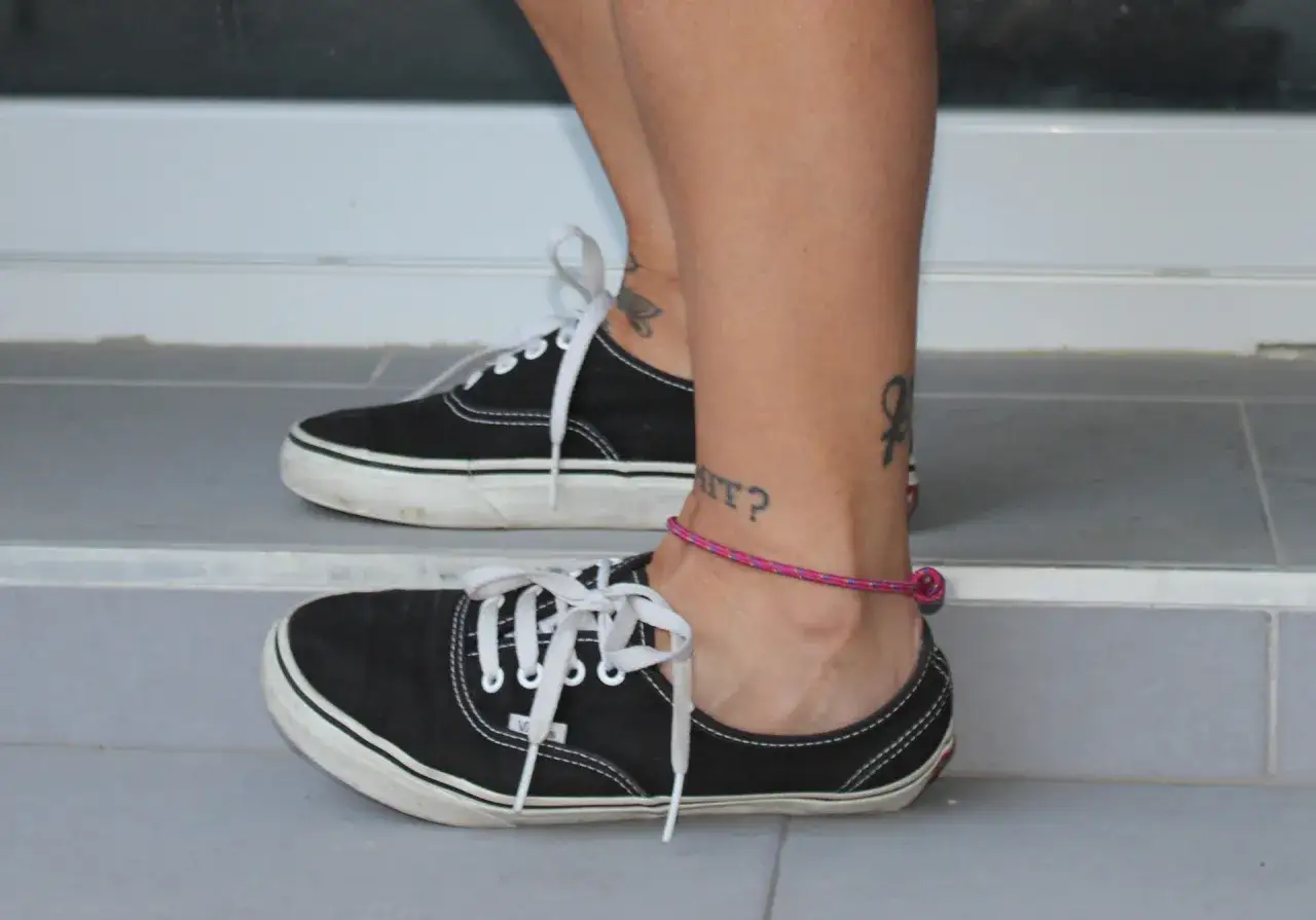 Calzado para tendinitis peroneos: zapatillas negras con cordones blancos y tobillera rosa.