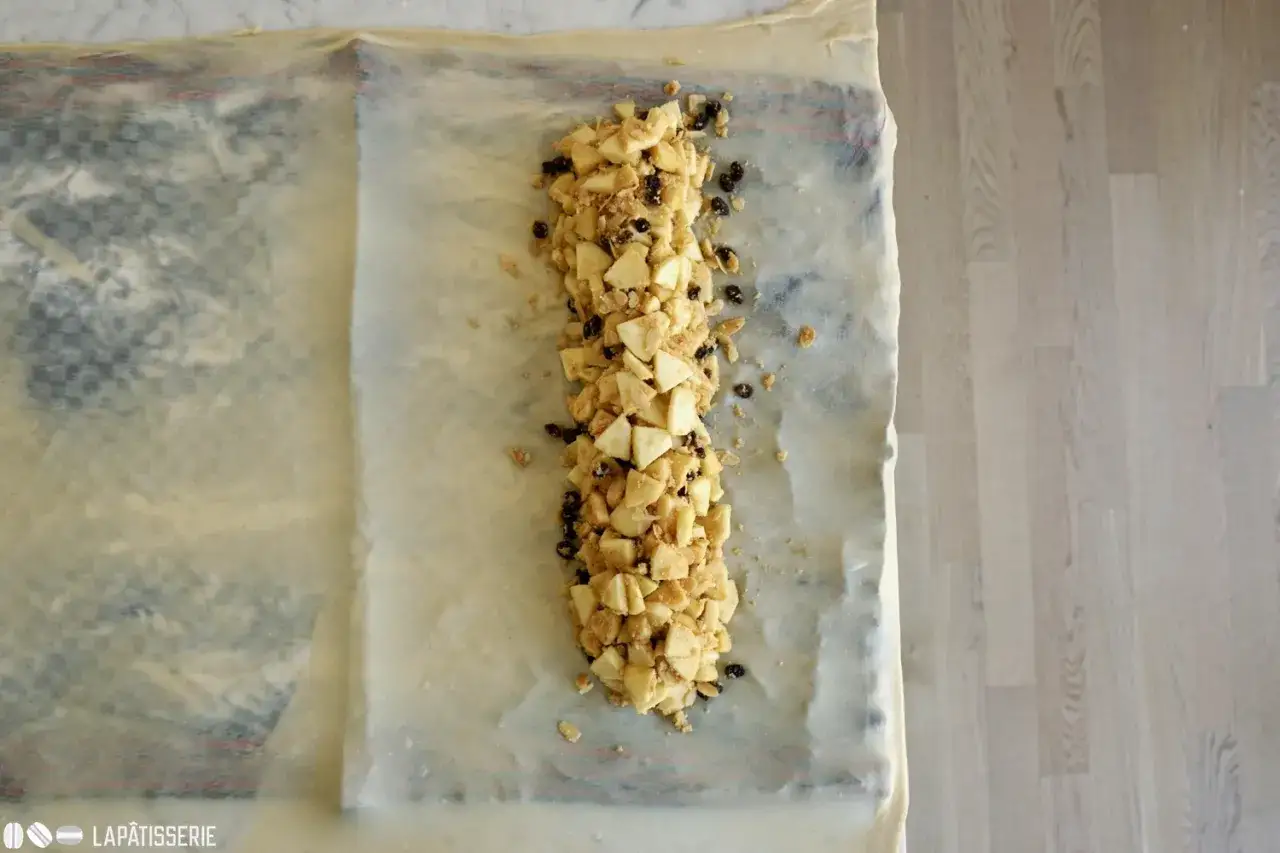 Apfelstrudel rezept: Äpfel und Rosinen liegen auf dünnem Teig, bereit zum Einrollen.