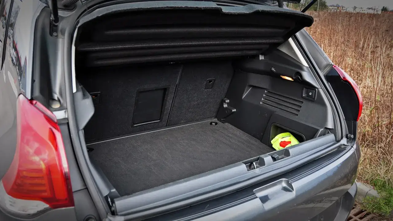 Bagażnik Peugeot 3008 2010, gotowy na podróż. W rogu schowany zielony pokrowiec z kamizelką odblaskową.