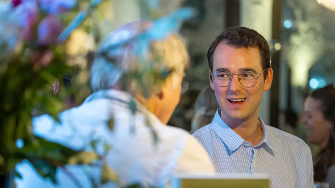 Johan Kellman Larsson ler och pratar med någon vid ett bord, med blommor i förgrunden.