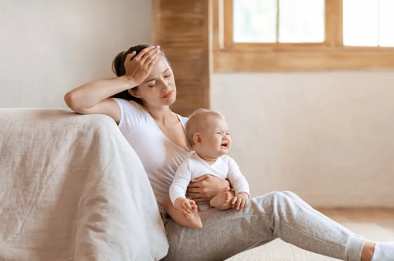Zmęczona mama z dzieckiem na rękach, kt&oacute;re płacze. Widać skutki częstego płaczu i wyczerpania.