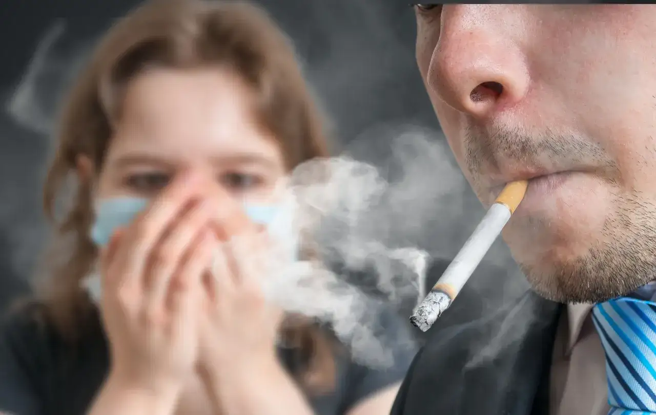 Persona con mascarilla se tapa la nariz por el humo de un cigarrillo. Aprende como quitar el olor a tabaco de la casa.