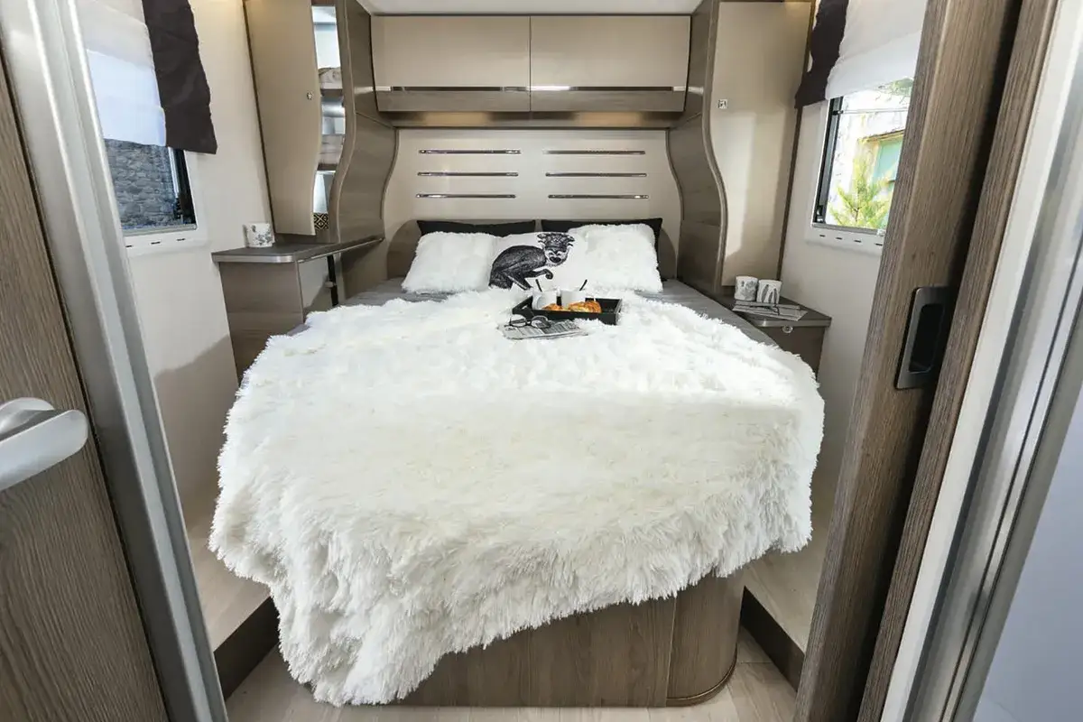 Un lit douillet dans un plan camping-car, pr&ecirc;t pour une nuit paisible. Une couverture moelleuse et des coussins invitent au repos.