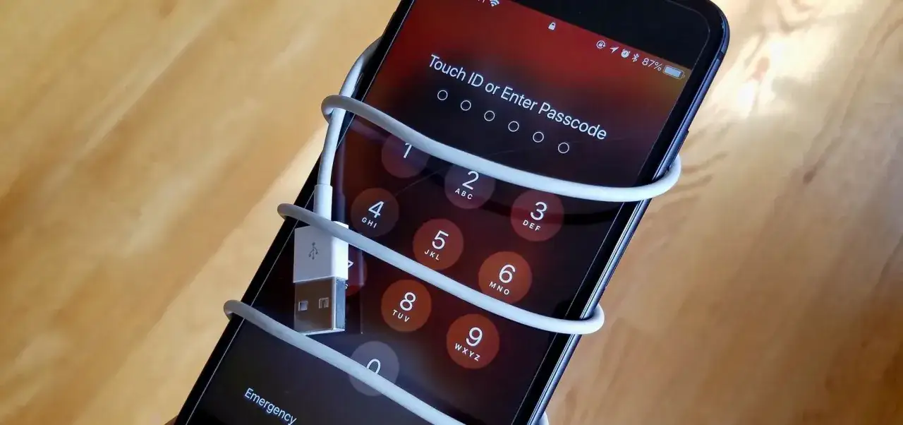 iPhone zablokowany, ekran z prośbą o podanie kodu. Kabel USB oplata telefon, sugerując, jak odblokować iPhone.