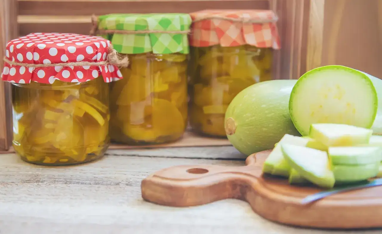 Gl&auml;ser mit eingelegtem Gem&uuml;se, bereit zum **Zucchini fermentieren**. Frische Zucchini liegen daneben auf einem Holzbrett.