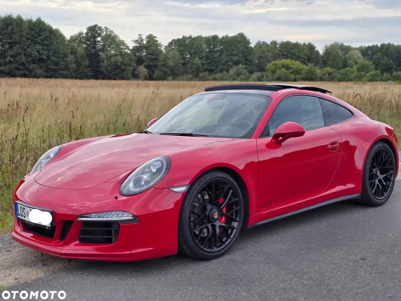 Czerwone Porsche 991 GTS z czarnymi felgami na tle pola i lasu.