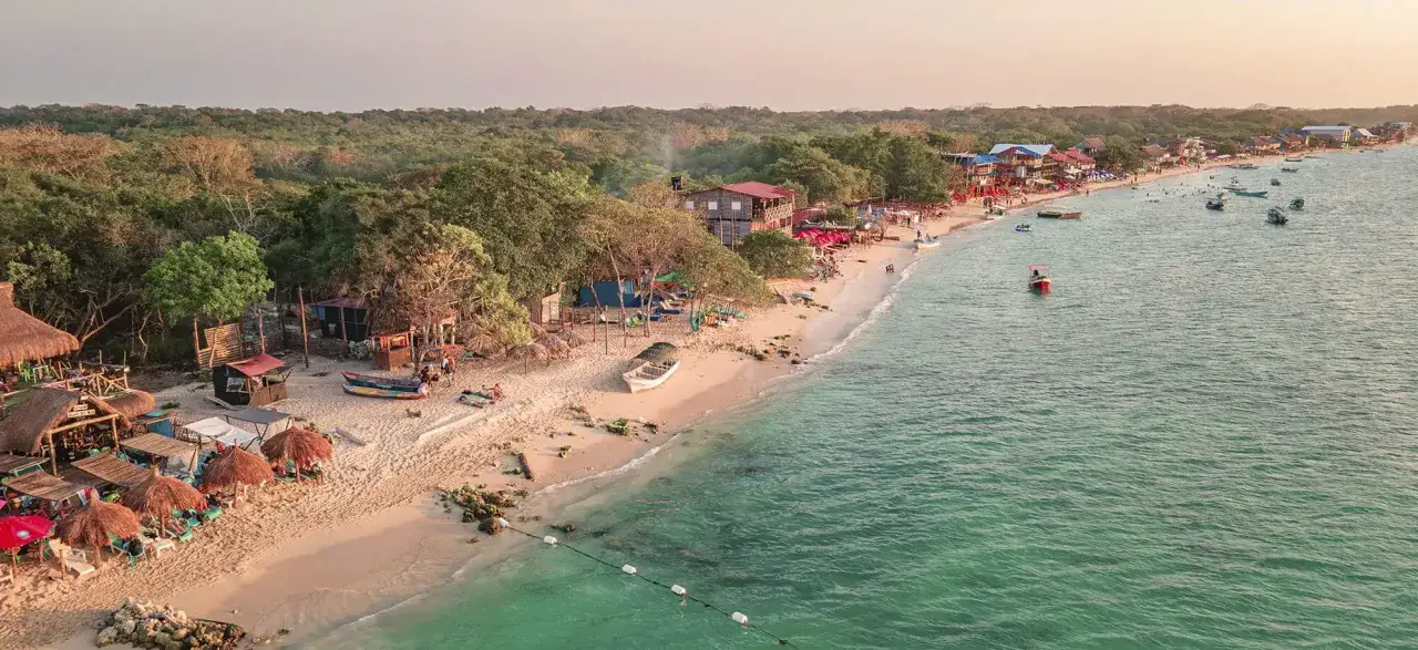 Playa caribeña con palapas, gente disfrutando y botes en el mar turquesa. ¡La mejor época para viajar a Colombia es ahora!