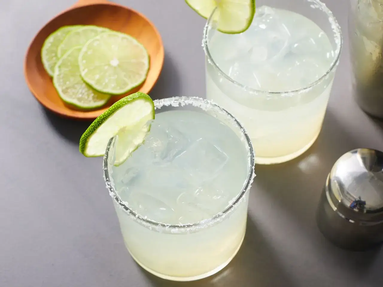 Dwa orzeźwiające drinki z lodem i solą na brzegu szklanki, udekorowane plasterkami limonki. Idealne na lato, przypominają o smaku likieru do margarity.