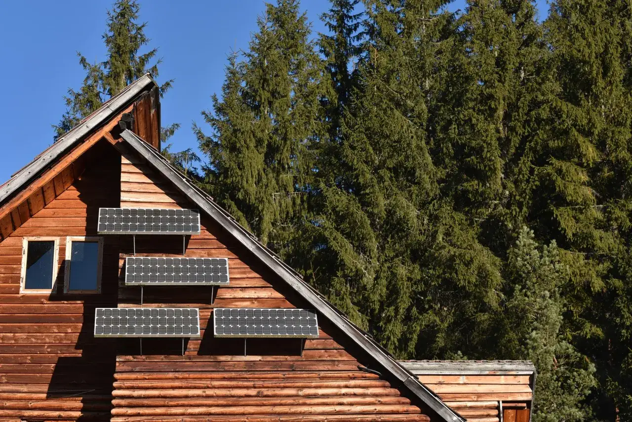Drewniany dom z panelami fotowoltaicznymi na ścianie. Czy instalacja fotowoltaiczna wymaga pozwolenia na budowę? W górach, wśród drzew, ekologiczne rozwiązanie.
