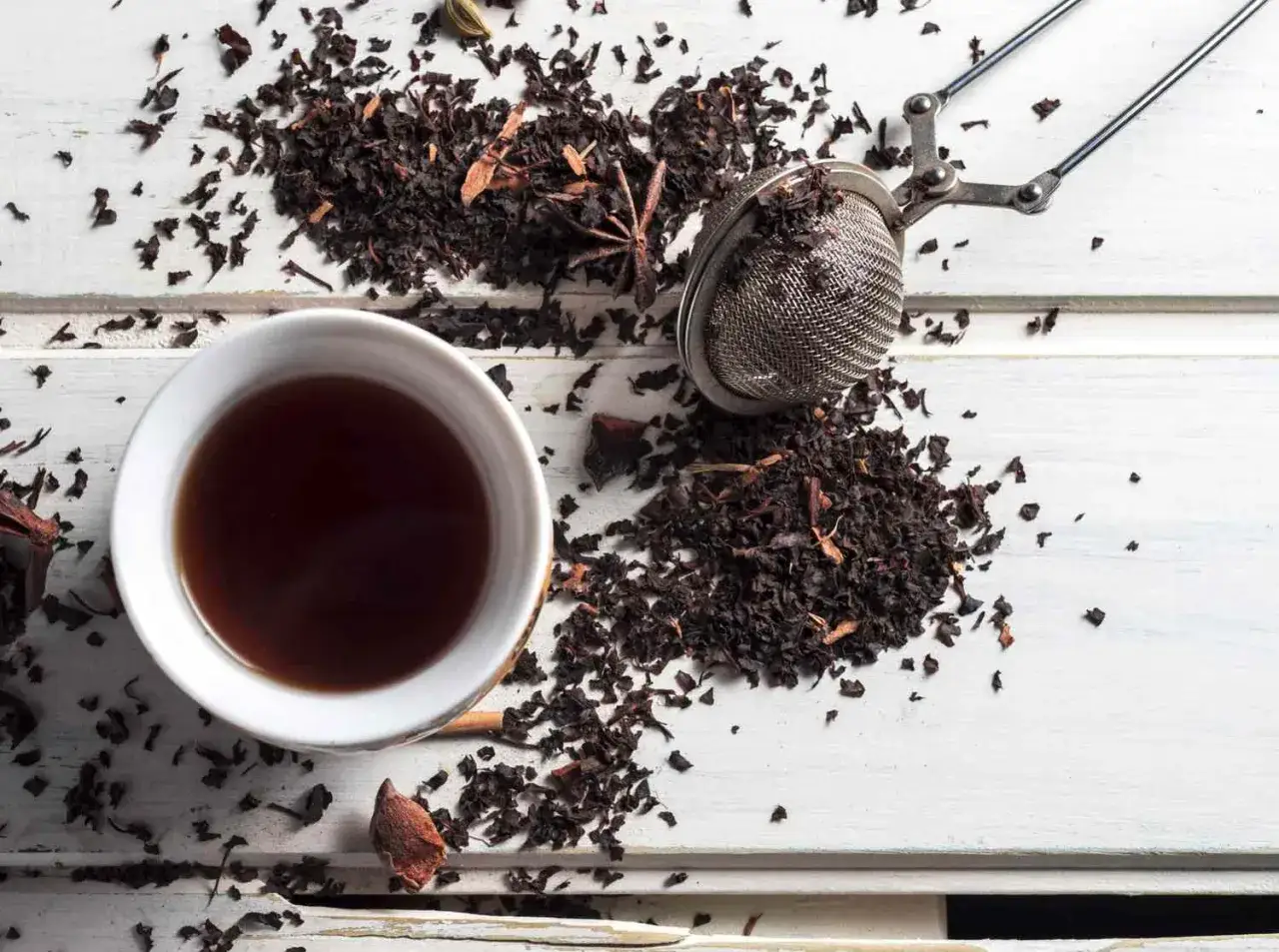 Aromatic czarna herbata w filiżance, obok zaparzacz i liście. Idealny czas parzenia czarnej herbaty to klucz do pełni smaku.