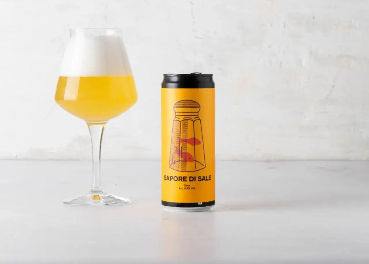 Bicchiere di birra dorata con schiuma bianca accanto a una lattina gialla con etichetta