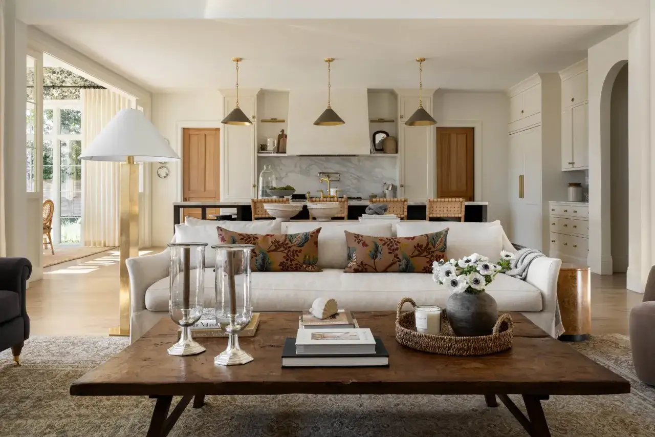 A living room with a neutral palette, featuring a plush sofa, a rustic coffee table, and a kitchen in the background, all embodying a chic McGee and Co style.