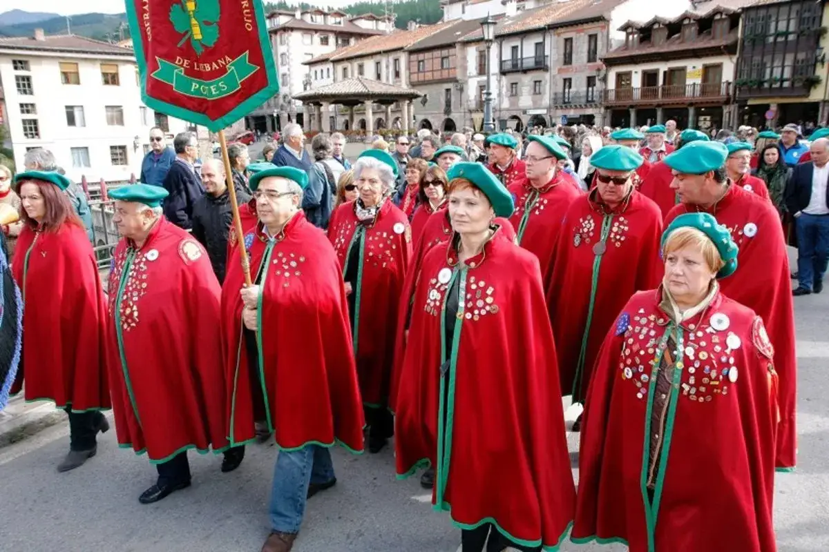 Gente con capas rojas y boinas verdes desfila en la fiesta del orujo Potes, portando un estandarte.