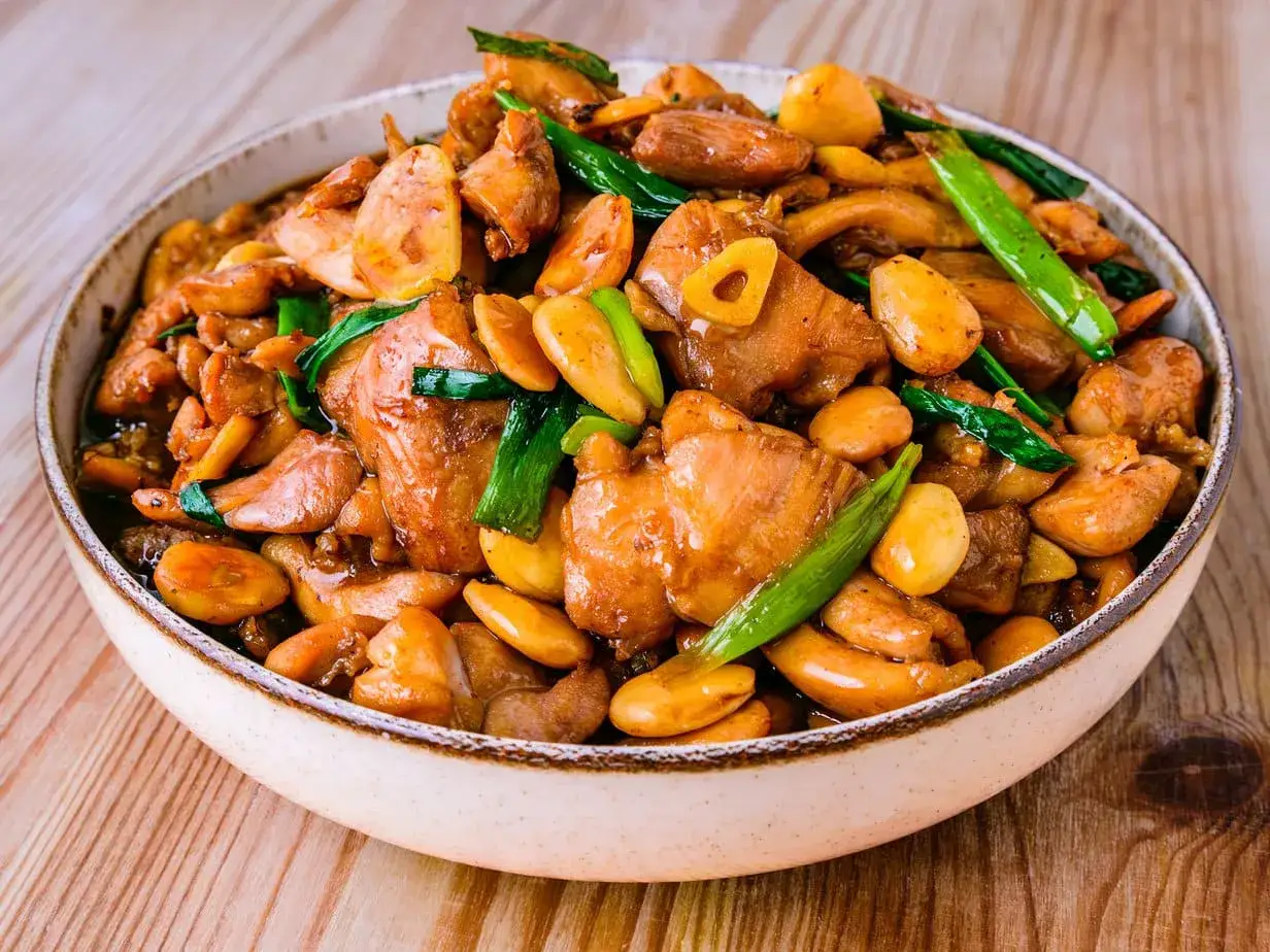 Un delicioso pollo con almendras, salteado con trozos de pollo tierno, almendras tostadas y cebolleta verde, servido en un cuenco rústico.