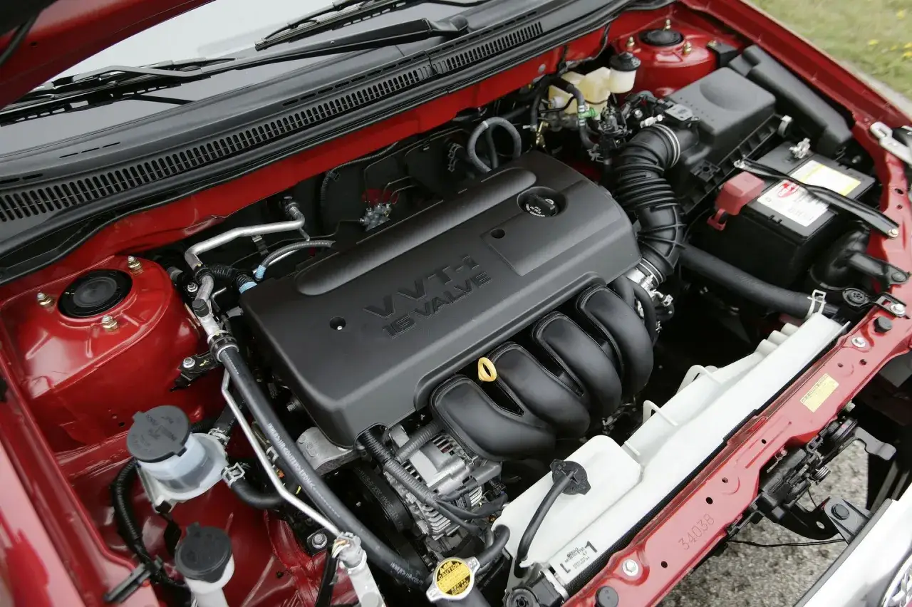 Silnik VVT-i 16 Valve w czerwonej Toyota Corolla Verso. Widoczny akumulator i elementy układu chłodzenia.