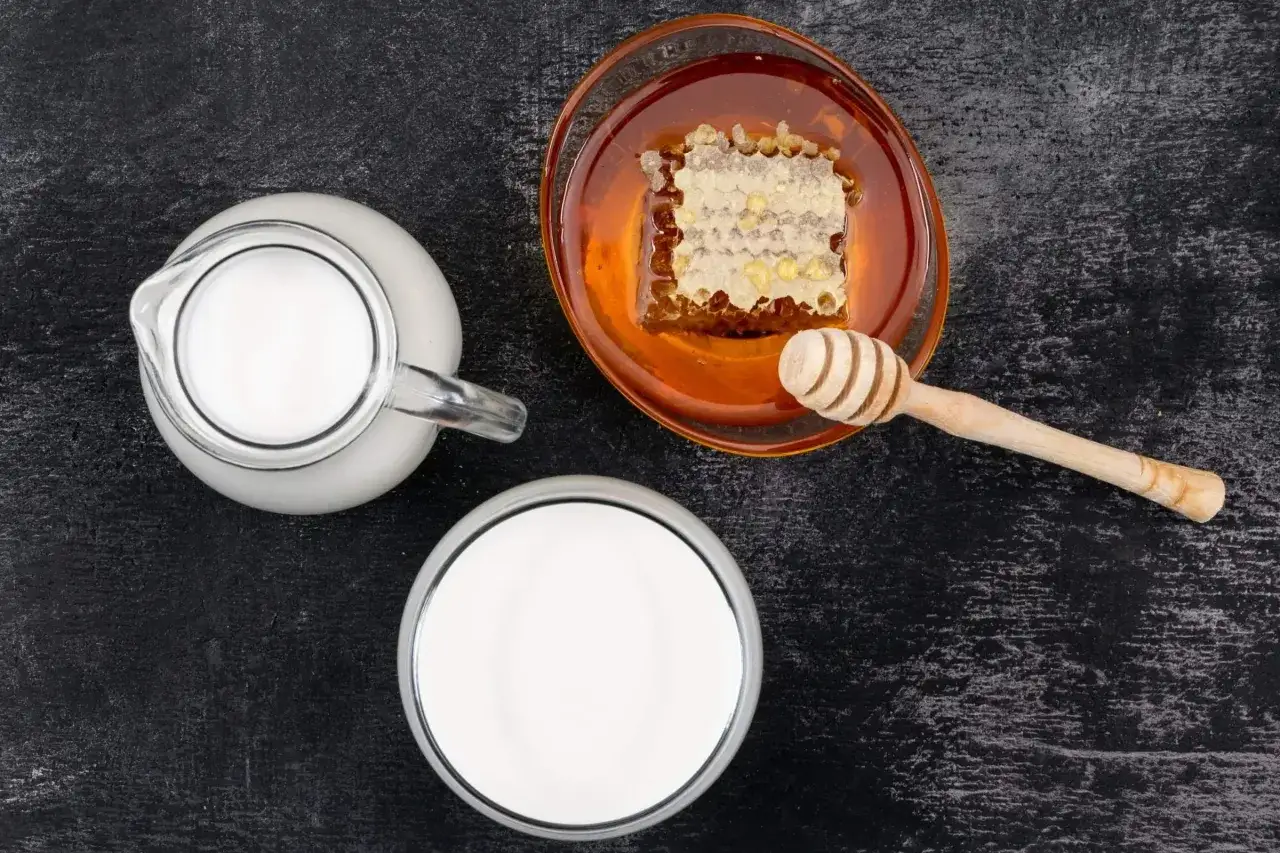 Caraffa e bicchiere di latte, ciotola di miele con favo e mestolo. Alcuni credono che latte caldo e miele faccia male, ma è un rimedio popolare.