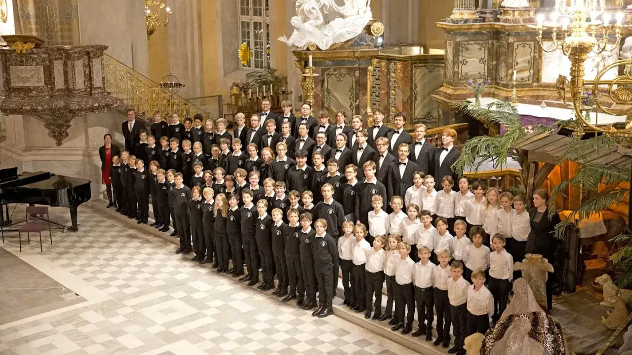Stor barnkör uppklädd i svarta dräkter i en av kyrkorna i Stockholm. En julkrubba syns i bakgrunden.