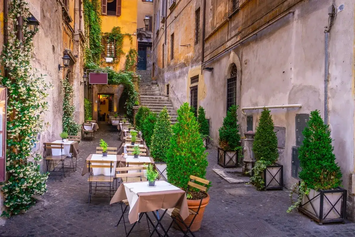 Un vicolo fiorito a Trastevere, con tavolini apparecchiati per un pasto all'aperto. Perfetto per scoprire cosa fare a Trastevere.