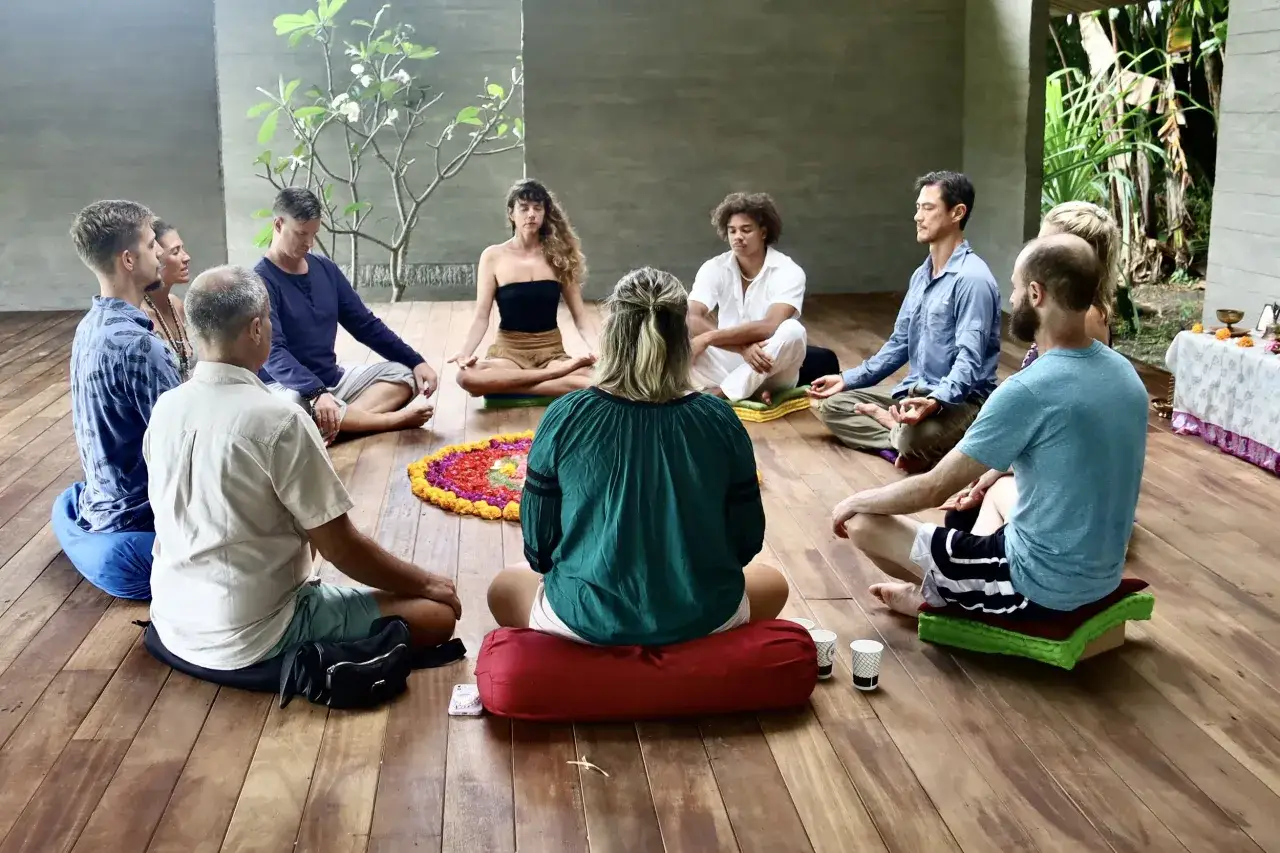 Menschen sitzen im Kreis auf dem Boden, umgeben von einer Blumenmandala. Sie scheinen an einer Meditationssitzung teilzunehmen, vielleicht für einen Ayurveda Podcast.