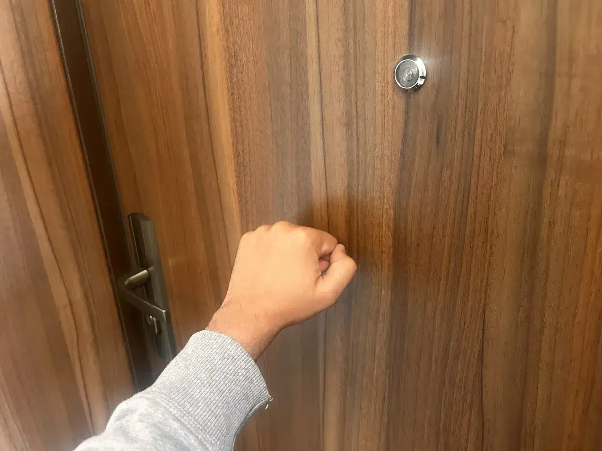 Dłoń puka do drzwi. Czy właściciel mieszkania odpowiada za lokatora?