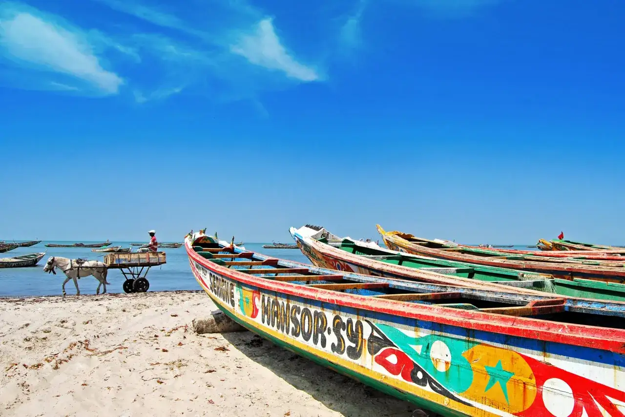 Kolorowe łodzie rybackie na plaży, koń ciągnie wózek z rybakiem. Idealne wakacje w Senegalu.