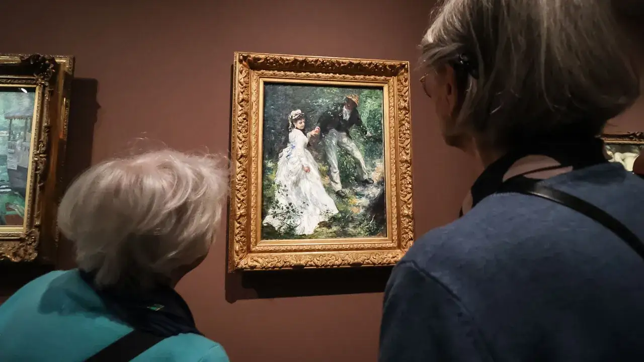 Deux personnes admirent une peinture de Renoir représentant un couple dans un jardin.
