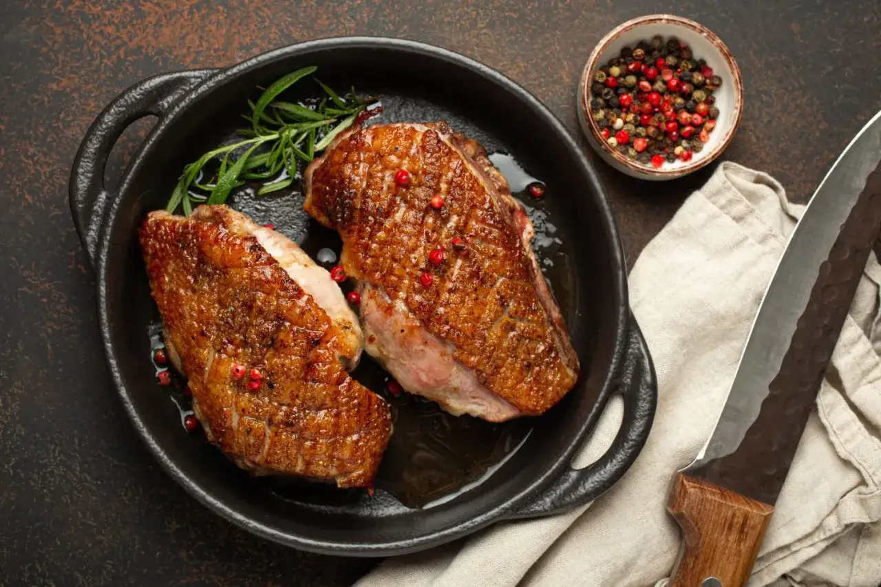 Zwei perfekt gebratene Entenbrustfilets in einer Pfanne, garniert mit Rosmarin und rosa Pfeffer. Ein k&ouml;stliches Entenfilet Rezept, bereit zum Servieren.