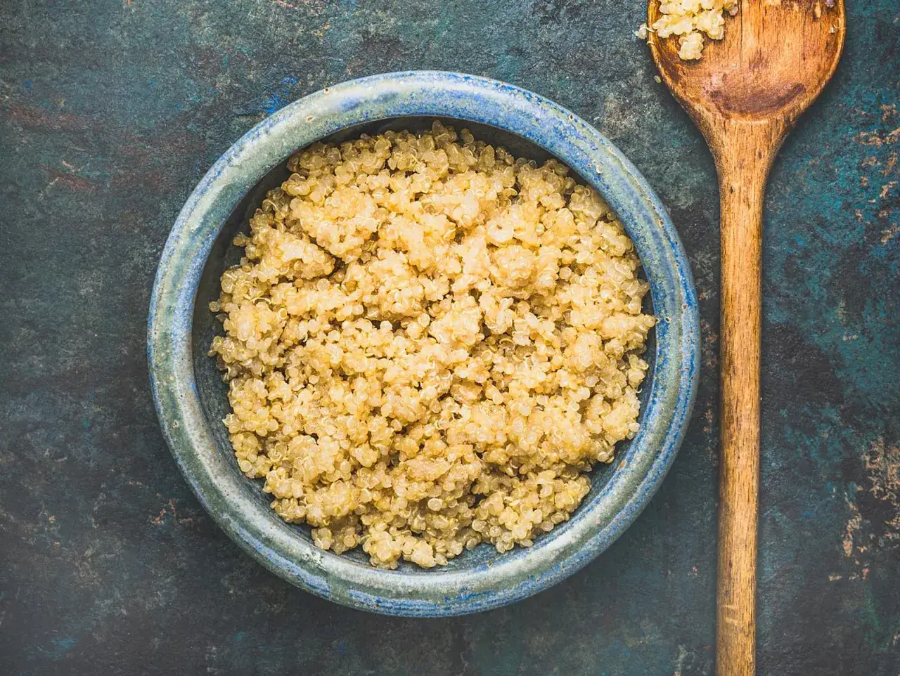 Gekochtes Quinoa in einer blauen Sch&uuml;ssel, daneben ein Holzl&ouml;ffel. Perfekt f&uuml;r gesundes Kochen.