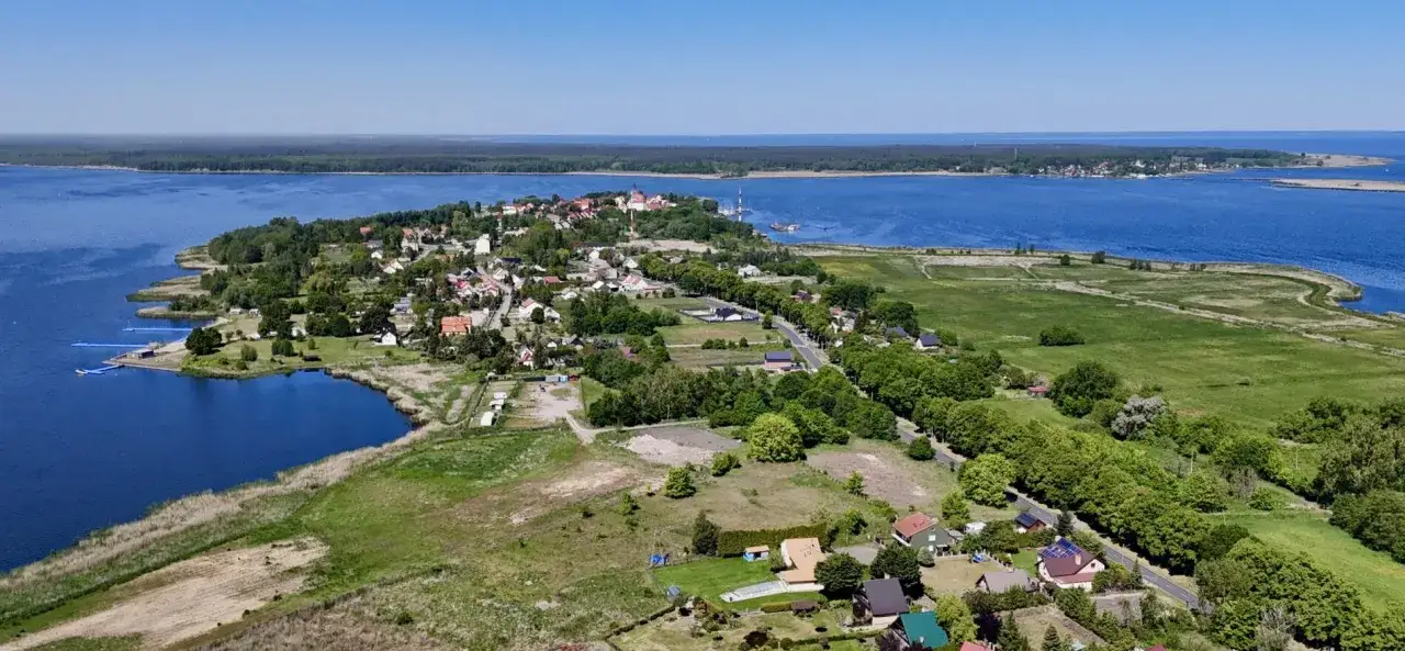 Widok na Nowe Warpno z lotu ptaka. Widać jezioro, zabudowania, las i zielone pola. Idealne miejsce na wypoczynek nad wodą.