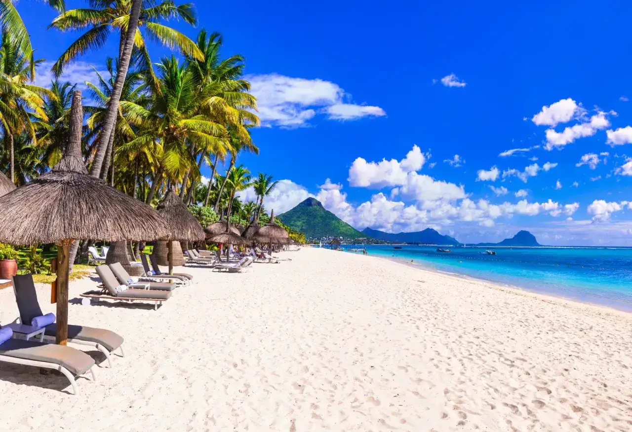 Traumhafter Strand auf Mauritius im Juli. Palmen, Liegestühle und das türkisfarbene Meer laden zum Entspannen ein. Perfektes Wetter für einen Urlaub.