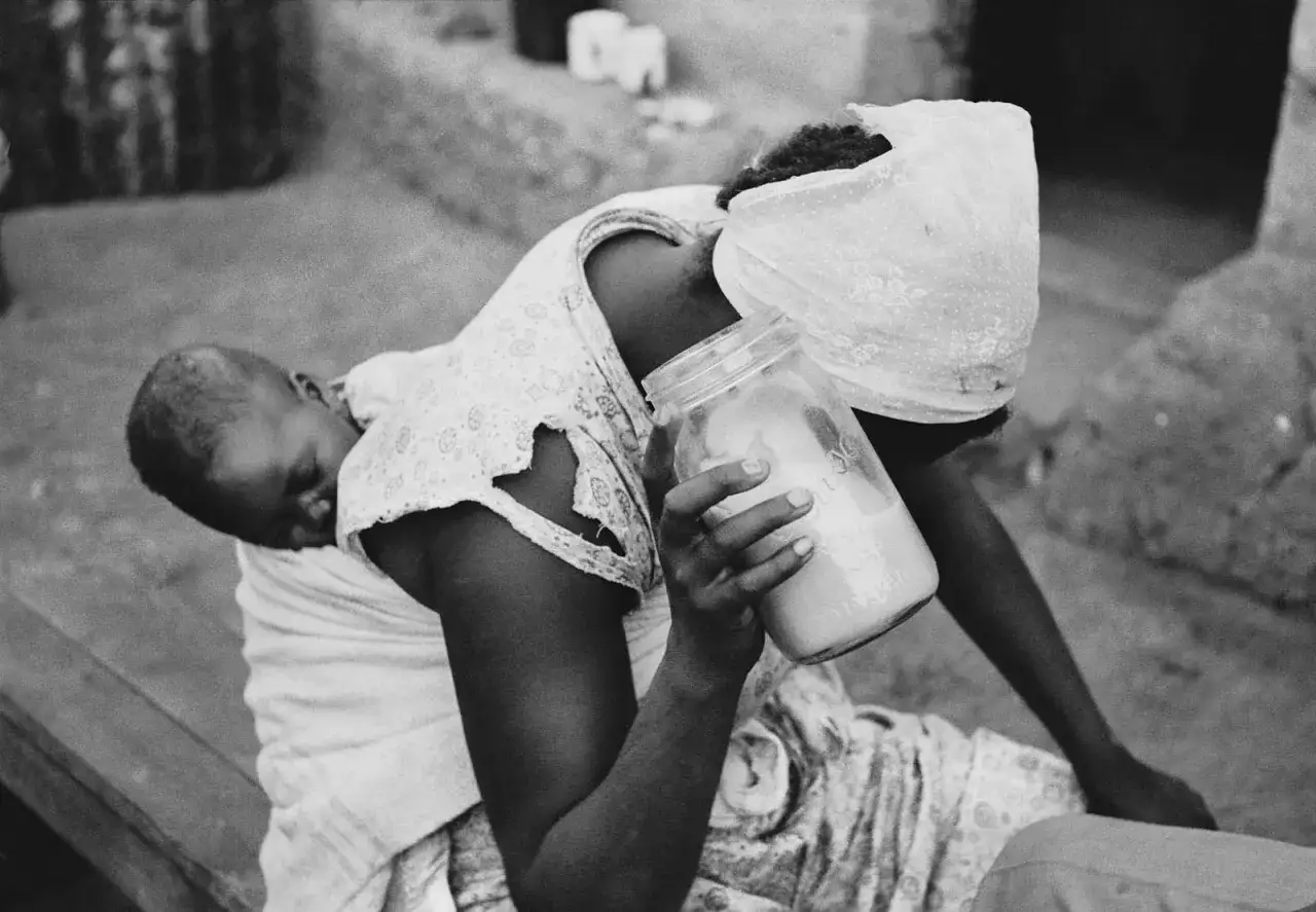 Persone in Sudafrica, una donna con un bambino in braccio tiene un barattolo di vetro con un liquido lattiginoso.