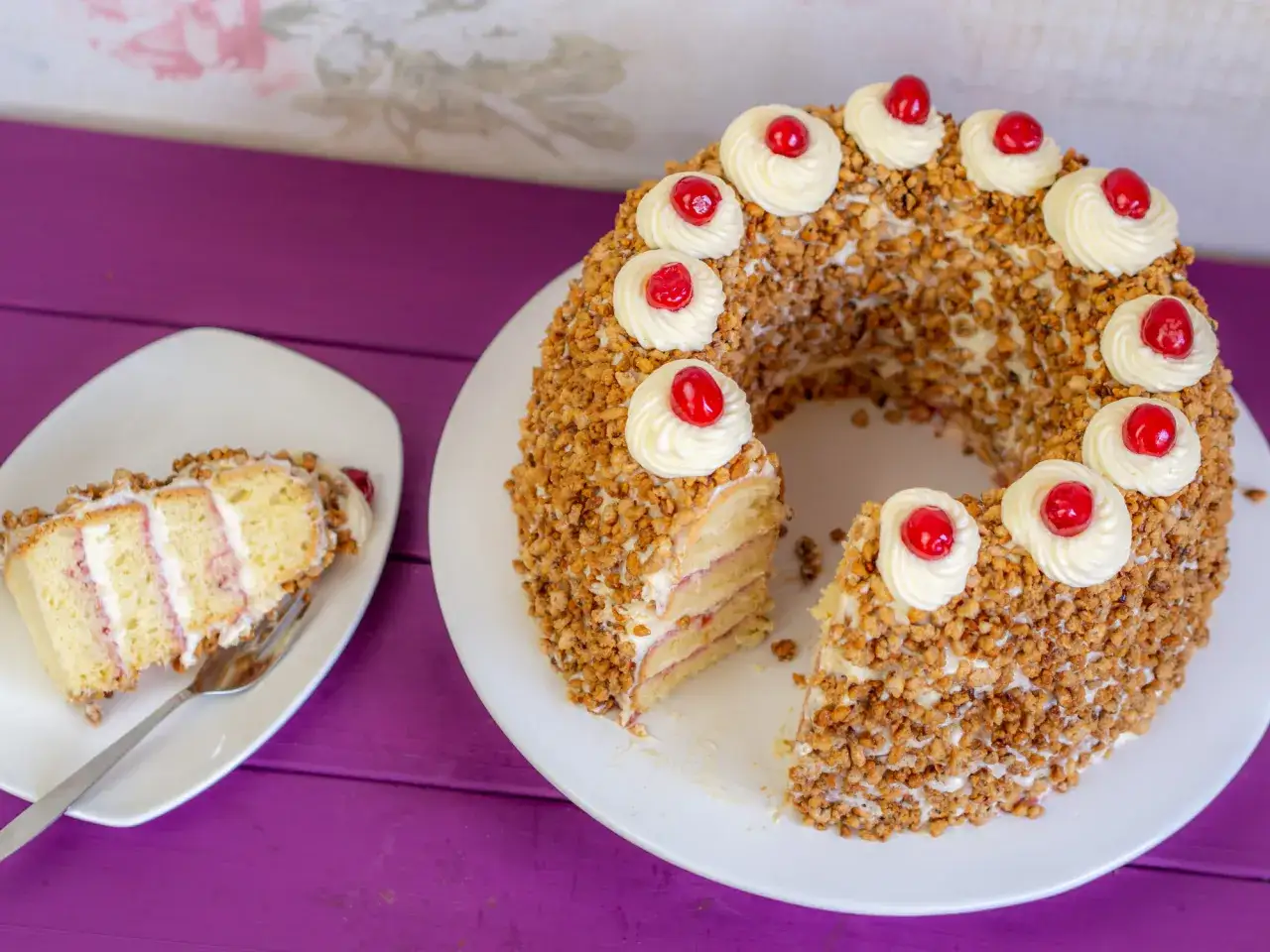 Ein k&ouml;stlicher Frankfurter Kranz, umh&uuml;llt von N&uuml;ssen und verziert mit Sahnetuffs und Kirschen. Ein St&uuml;ck ist bereits angeschnitten.