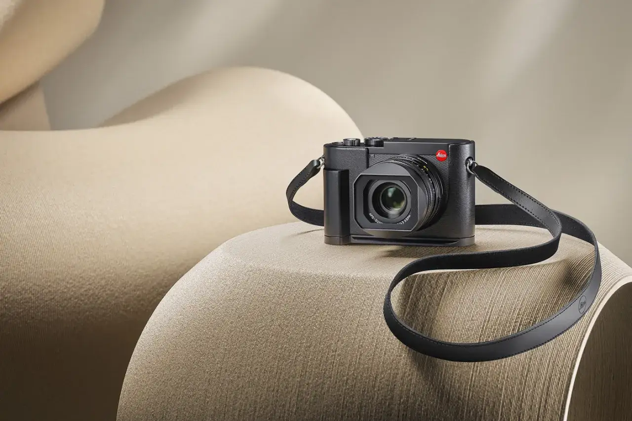 Un Leica Q3 noir, prêt pour un test, repose sur un fauteuil beige aux formes douces.