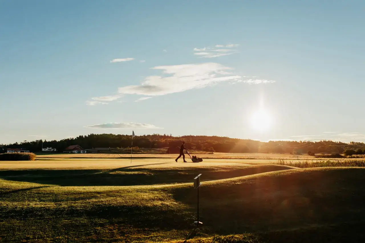 En person klipper gr&auml;set p&aring; en golfbana i solnedg&aring;ngen. En myra golf-dag i Sverige.