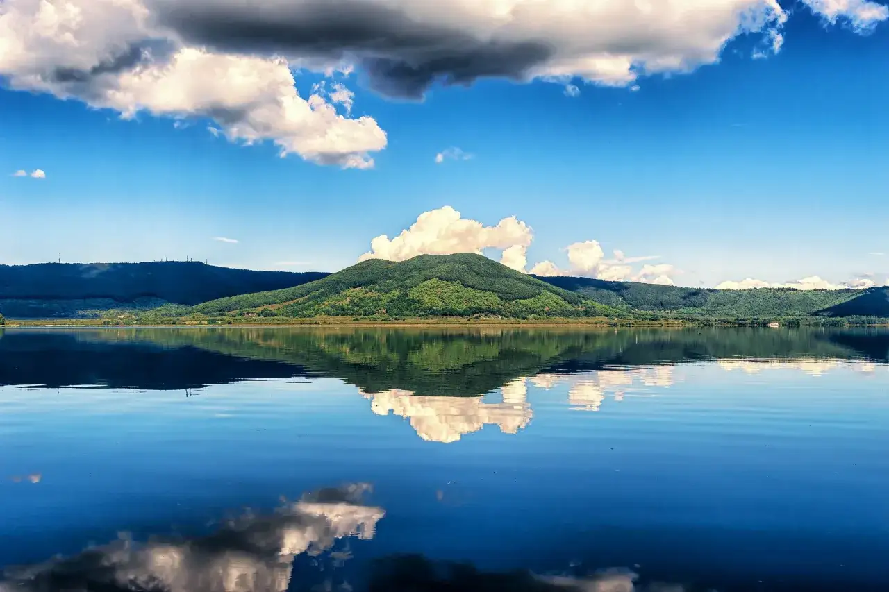Un lago calmo riflette colline verdi e nuvole bianche. Una vista incantevole del **bella Venere lago di Vico**.